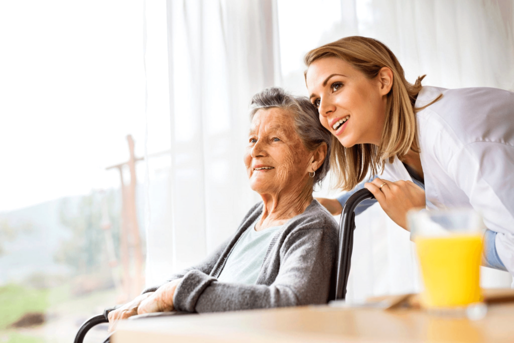 A nurse provides assistance to an elderly woman in a wheelchair at an assisted living facility.