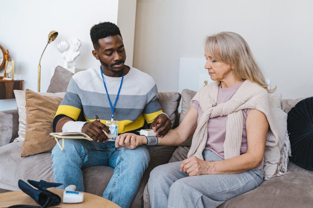 At Hampton Manor in Ocala, FL, a man provides compassionate care by measuring an elderly woman's blood pressure as they sit comfortably on the sofa, embodying the essence of assisted living.